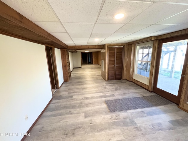 hall with a drop ceiling, baseboards, and light wood finished floors