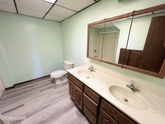 full bath with toilet, wood finished floors, a drop ceiling, and a sink