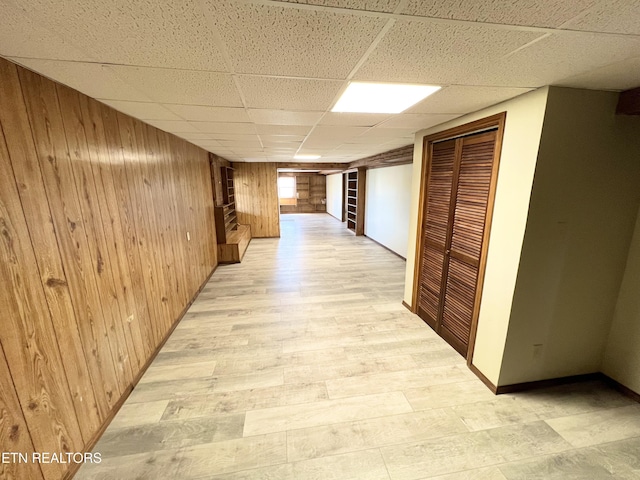 hall featuring a drop ceiling, wood walls, and light wood finished floors