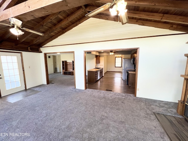 unfurnished living room featuring lofted ceiling with beams, wooden ceiling, ceiling fan, and dark carpet