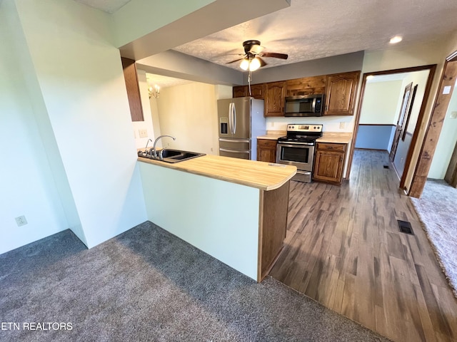 kitchen featuring visible vents, dark wood finished floors, a peninsula, a sink, and appliances with stainless steel finishes