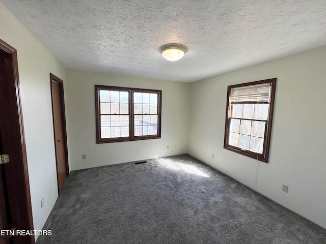 unfurnished room with visible vents, carpet floors, and a textured ceiling