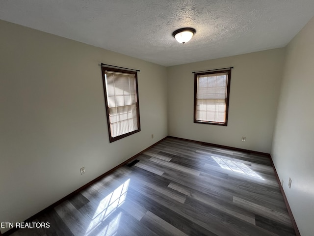 empty room featuring a wealth of natural light, a textured ceiling, baseboards, and wood finished floors