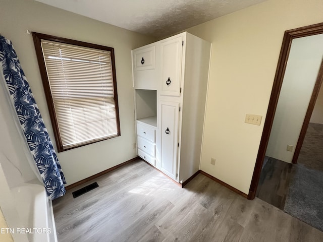 unfurnished bedroom featuring light wood-type flooring, visible vents, baseboards, and a textured ceiling