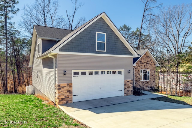 exterior space featuring concrete driveway, stone siding, a front yard, and roof with shingles