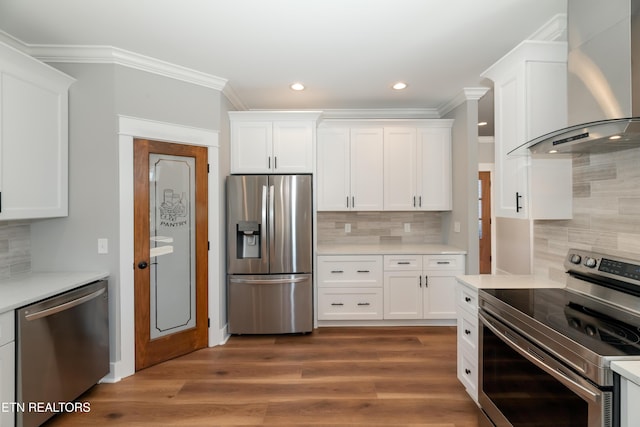 kitchen with light countertops, wall chimney exhaust hood, crown molding, and appliances with stainless steel finishes