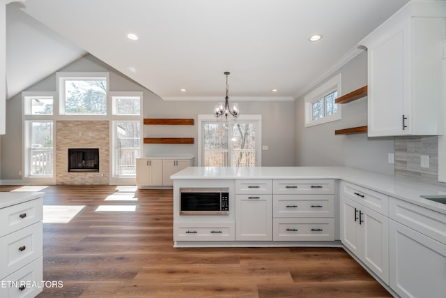 kitchen with open shelves, stainless steel microwave, a peninsula, and a tile fireplace