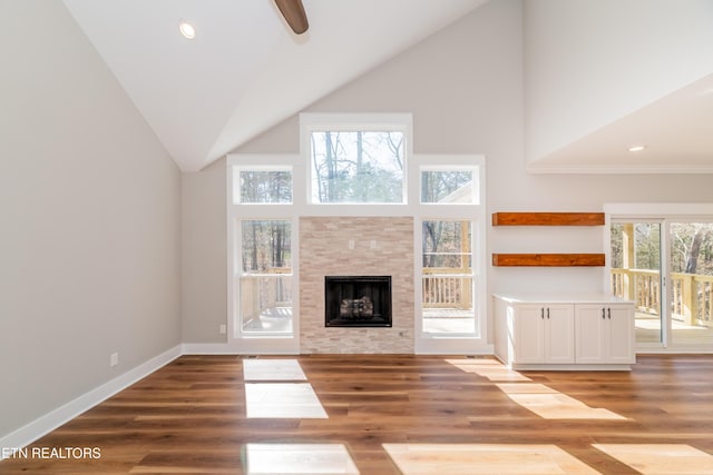 unfurnished living room featuring ceiling fan, baseboards, a tile fireplace, wood finished floors, and high vaulted ceiling