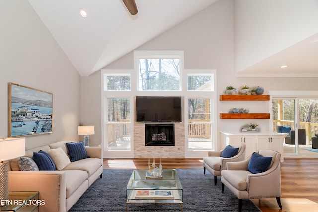 living area with a tiled fireplace, recessed lighting, high vaulted ceiling, and wood finished floors