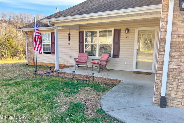 doorway to property featuring a yard, covered porch, and a shingled roof