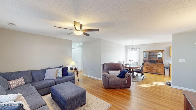 living room featuring visible vents, ceiling fan with notable chandelier, a textured ceiling, light wood finished floors, and baseboards