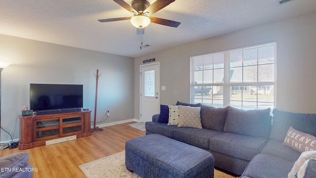 living room with light wood finished floors, visible vents, baseboards, ceiling fan, and a textured ceiling