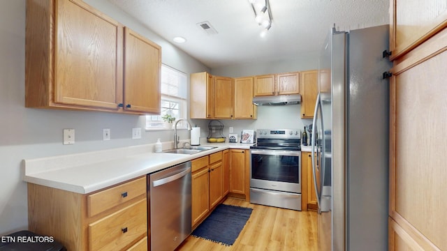 kitchen featuring visible vents, under cabinet range hood, light wood-style floors, stainless steel appliances, and a sink