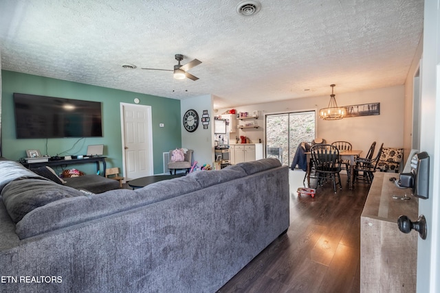 living area with visible vents, a textured ceiling, dark wood-style flooring, and ceiling fan with notable chandelier