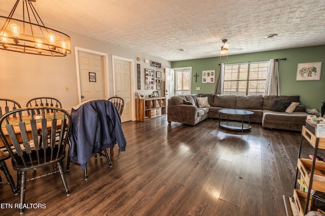 living room with ceiling fan with notable chandelier, a textured ceiling, and dark wood-type flooring