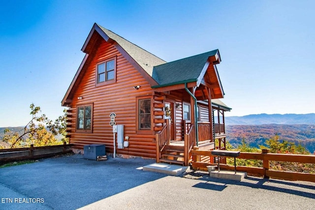 exterior space featuring log siding, roof with shingles, a mountain view, and fence