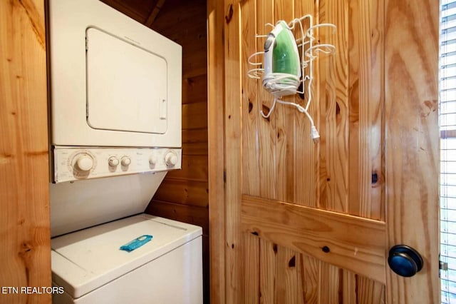 laundry room with laundry area, wood walls, and stacked washer and dryer