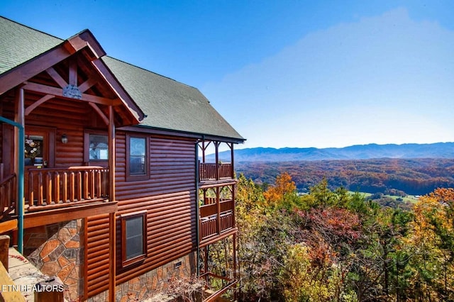 view of home's exterior featuring a balcony, a mountain view, log veneer siding, and roof with shingles