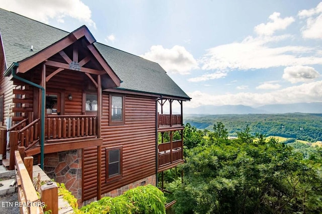 view of property exterior with a balcony, a mountain view, and roof with shingles