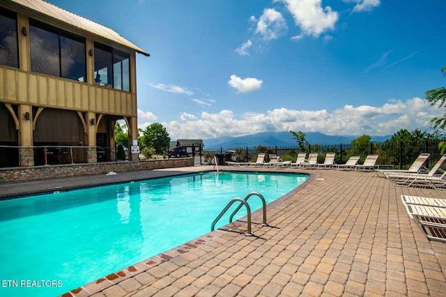 pool with a patio area, a mountain view, and fence