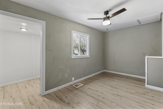 spare room with a ceiling fan, wood finished floors, visible vents, baseboards, and attic access