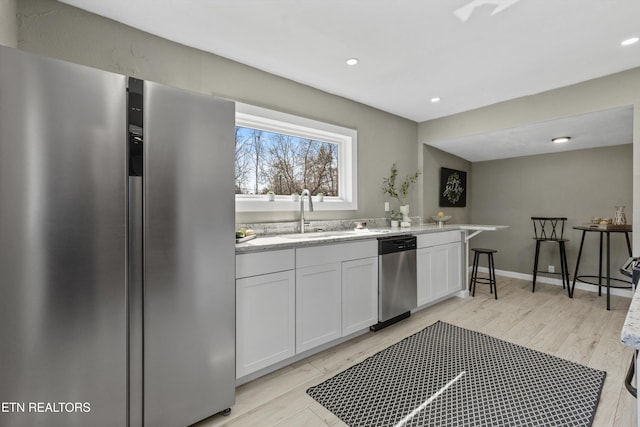 kitchen with light stone countertops, a sink, light wood-style floors, appliances with stainless steel finishes, and white cabinetry