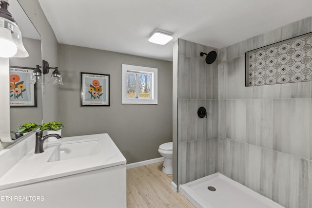 bathroom with vanity, wood finished floors, baseboards, a tile shower, and toilet