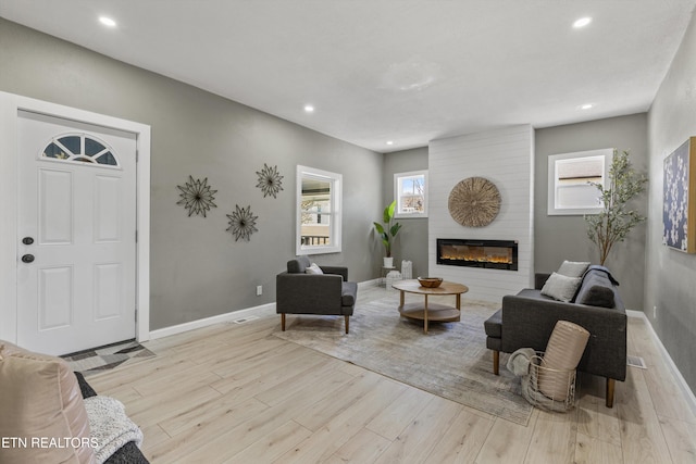 living room featuring recessed lighting, baseboards, a large fireplace, and wood finished floors