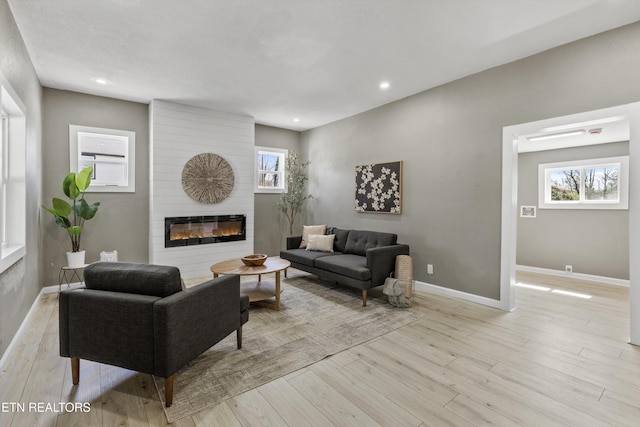 living area with recessed lighting, a fireplace, baseboards, and light wood finished floors