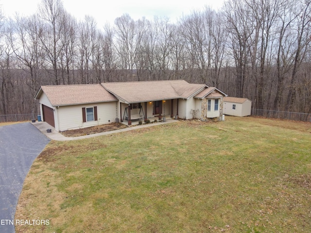 ranch-style home featuring a front lawn, fence, covered porch, a garage, and a storage unit