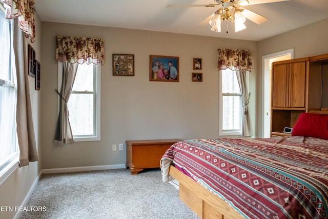 bedroom with ceiling fan, multiple windows, baseboards, and light carpet