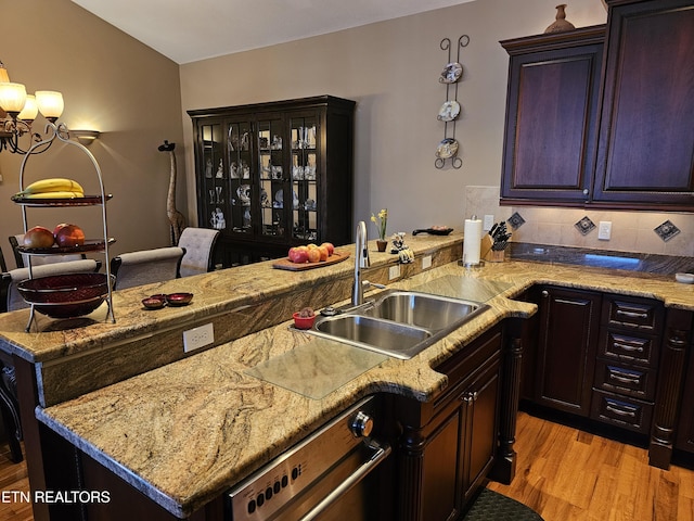 kitchen with a sink, light wood-type flooring, light stone countertops, and tasteful backsplash