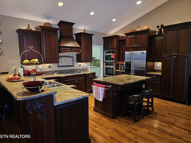 kitchen featuring light wood finished floors, premium range hood, a breakfast bar, lofted ceiling, and stainless steel appliances