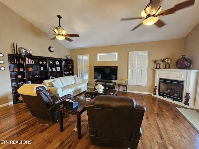 living area featuring a glass covered fireplace, vaulted ceiling, wood finished floors, and ceiling fan