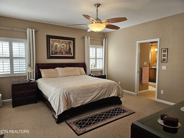 bedroom with connected bathroom, baseboards, light colored carpet, and a ceiling fan