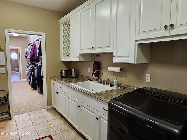 kitchen with a sink, washer / clothes dryer, white cabinets, light tile patterned flooring, and light colored carpet