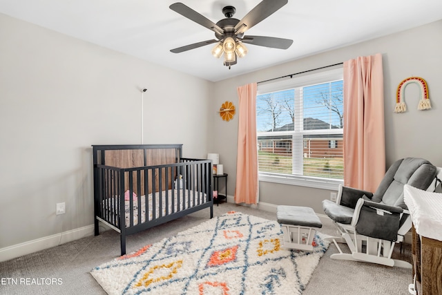 bedroom featuring a crib, a ceiling fan, baseboards, and carpet floors