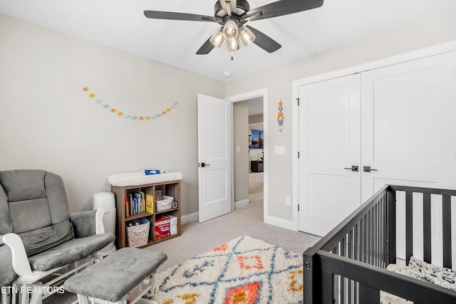 bedroom with a crib, light carpet, a closet, baseboards, and ceiling fan