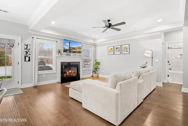 living area featuring visible vents, baseboards, a fireplace with flush hearth, ornamental molding, and wood finished floors