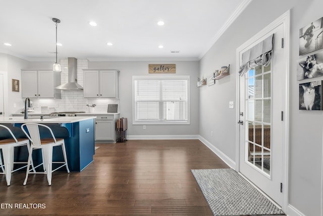 kitchen featuring a breakfast bar area, wall chimney exhaust hood, dark wood finished floors, and crown molding