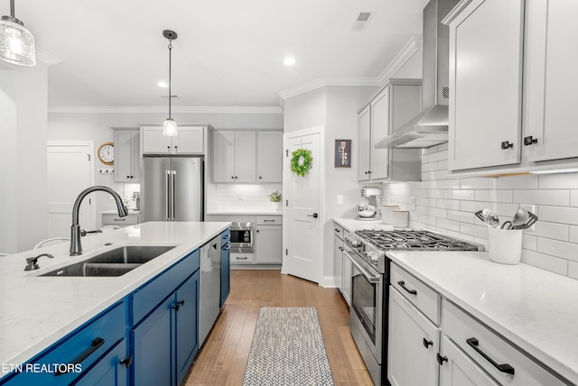 kitchen featuring stainless steel appliances, blue cabinets, wall chimney range hood, and a sink