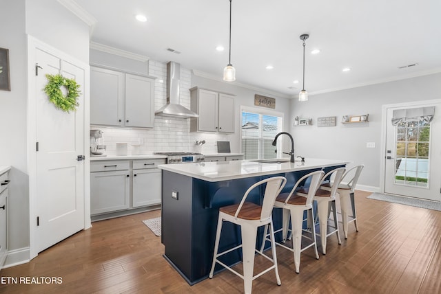 kitchen with dark wood-type flooring, a sink, wall chimney exhaust hood, crown molding, and decorative backsplash