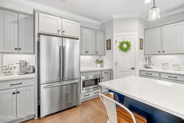 kitchen featuring gray cabinetry, ornamental molding, appliances with stainless steel finishes, a breakfast bar area, and light wood finished floors