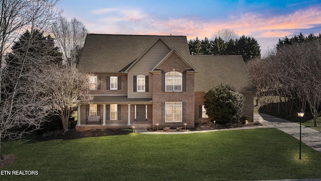 view of front facade featuring brick siding, a porch, a front yard, and a shingled roof