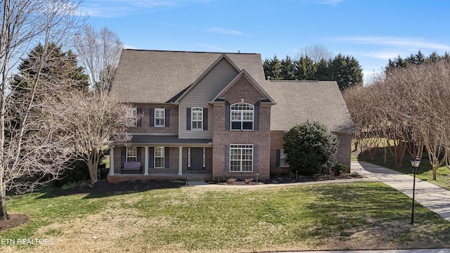 view of front facade with a front yard, roof with shingles, a porch, concrete driveway, and brick siding