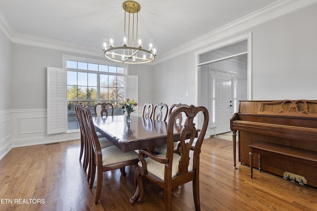 dining area featuring wainscoting, ornamental molding, an inviting chandelier, and wood finished floors