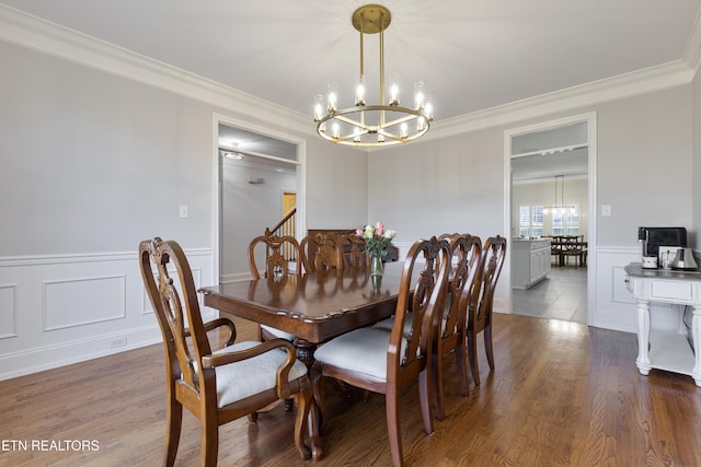 dining space with wood finished floors, a chandelier, wainscoting, and ornamental molding