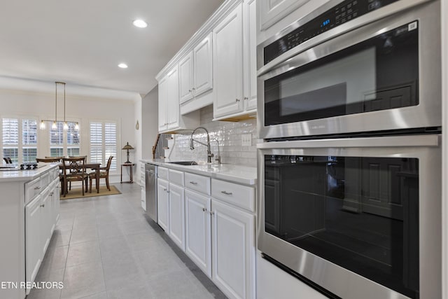 kitchen with tasteful backsplash, light countertops, stainless steel appliances, white cabinetry, and a sink