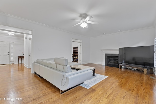 living area featuring light wood finished floors, baseboards, a tiled fireplace, ornamental molding, and a ceiling fan