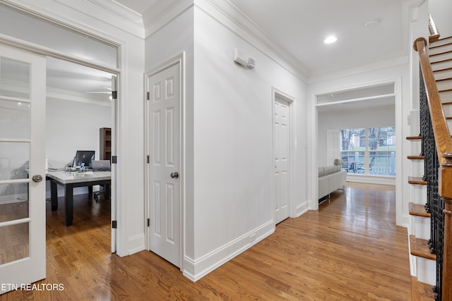 hallway featuring stairs, baseboards, light wood-style floors, and crown molding